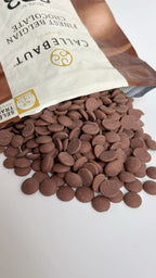 Callebaut  au lait chocolate chips spilling out of a bag on a white background