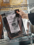 Hand holding a Callebaut chocolate package on a shelf with other chocolate products.
